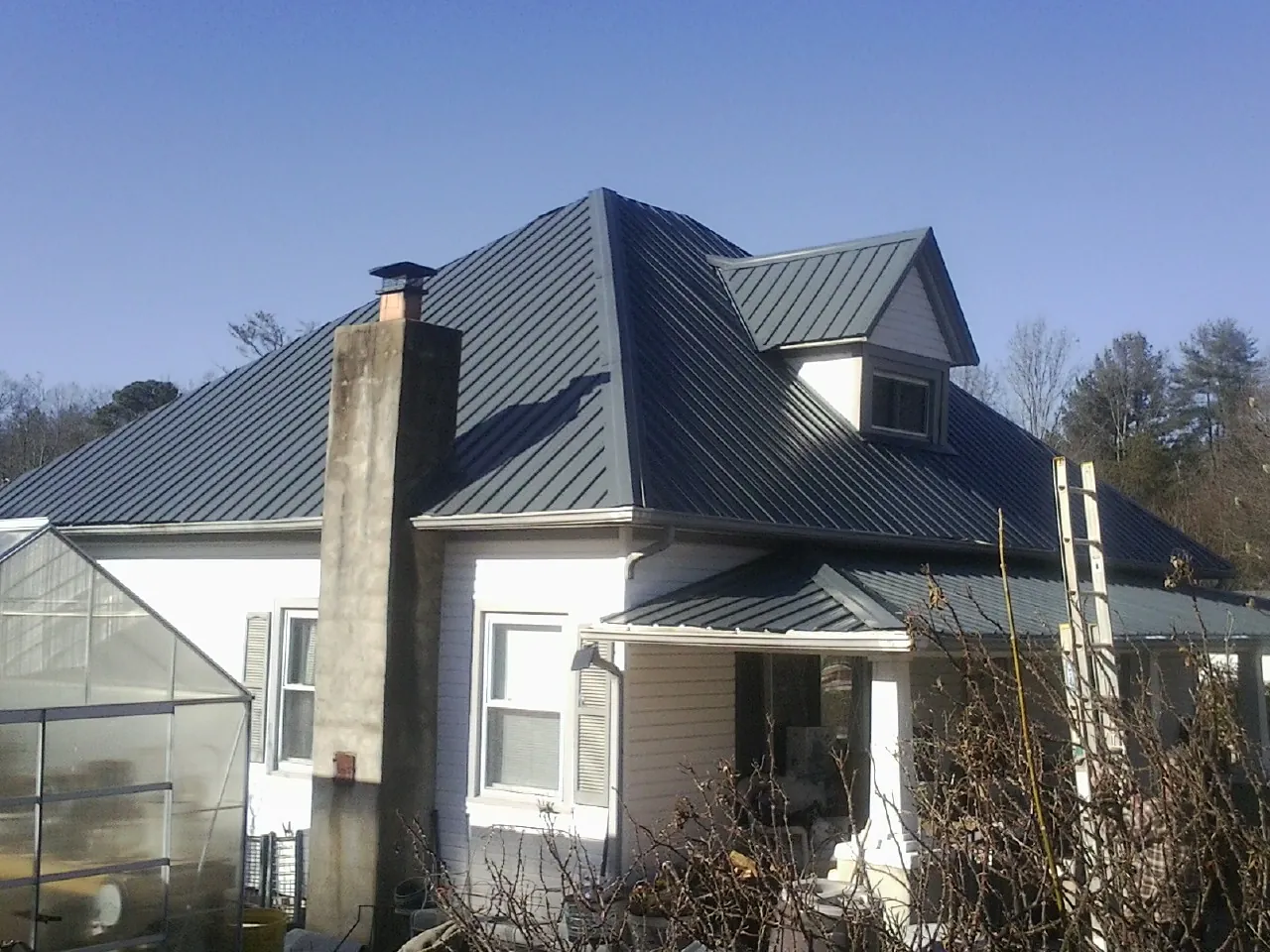 Dark blue standing seam metal roof on a white farmhouse with dormer — Slate & Tile Roof Repair by Roofing Brothers in Bunn