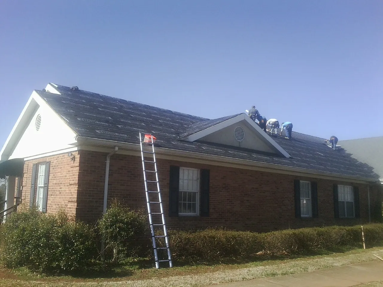 Crew tearing shingles off a brick ranch roof with a ladder set — Emergency Roof Repair work by our crew in Bunn