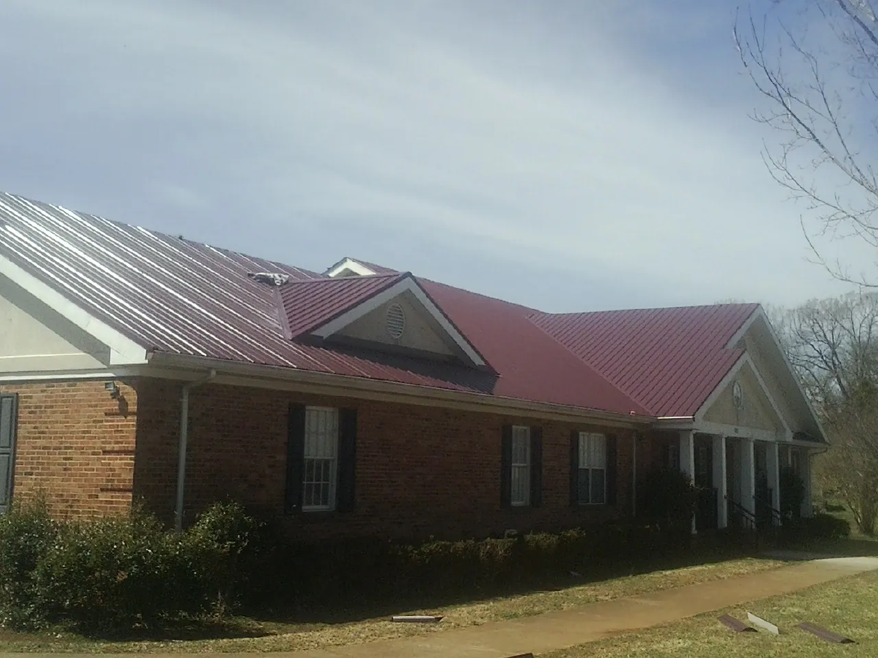 Red metal roof with gabled entries on a long brick building, from a Hail Damage Roof Repair job in Bunn