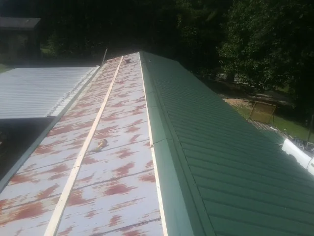 Old rusted panels beside newly installed green metal roofing — Wind Damage Roof Repair by Roofing Brothers in Bunn