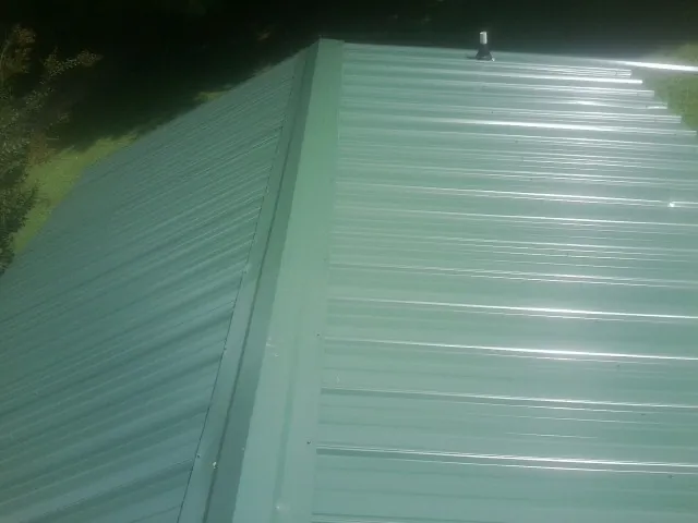 New green metal panels meeting at the ridge of a roof — Flat Roof Repair work by our crew in Bunn