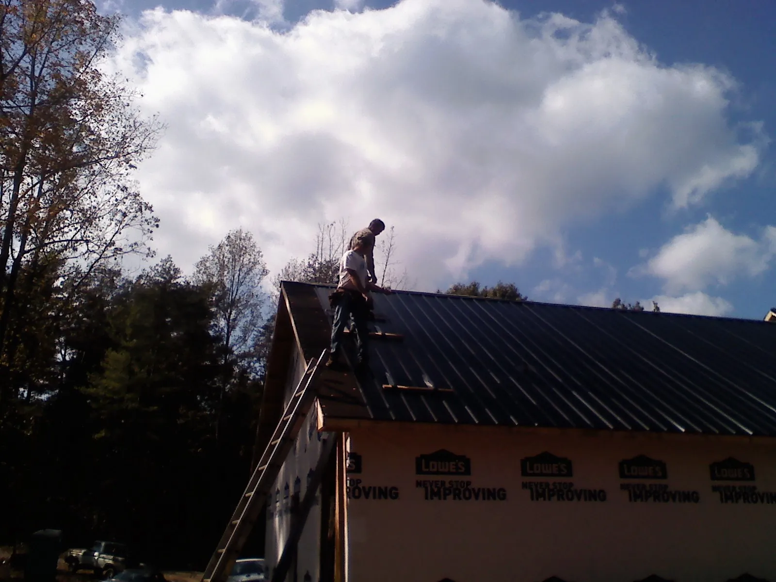 Roofer fastening dark metal panels high against a cloudy sky, from a Roof Inspection job in Bunn