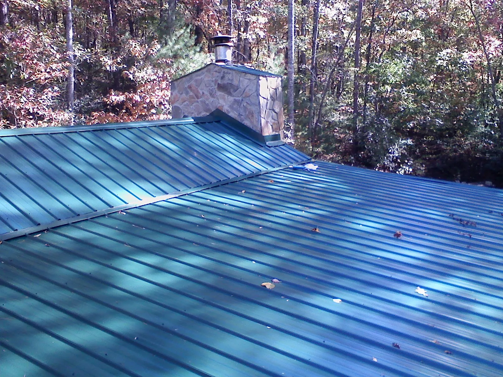 New green metal roof and stone chimney surrounded by autumn woods in Bunn