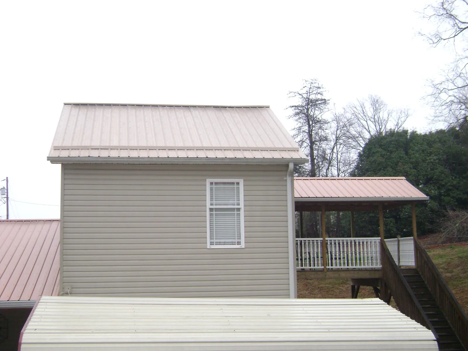 Tan metal roofs on a two story addition and attached porch, from a Roof Replacement job in Bunn